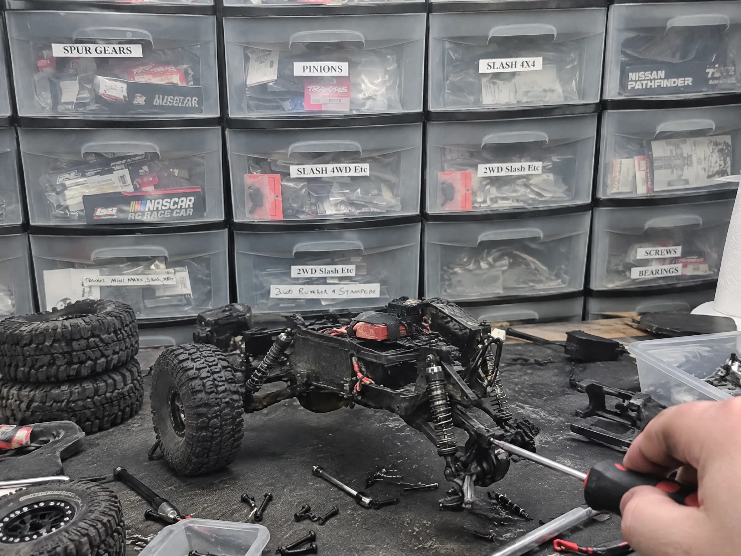 The repair bench: hands working on an RC crawler, parts drawers behind.